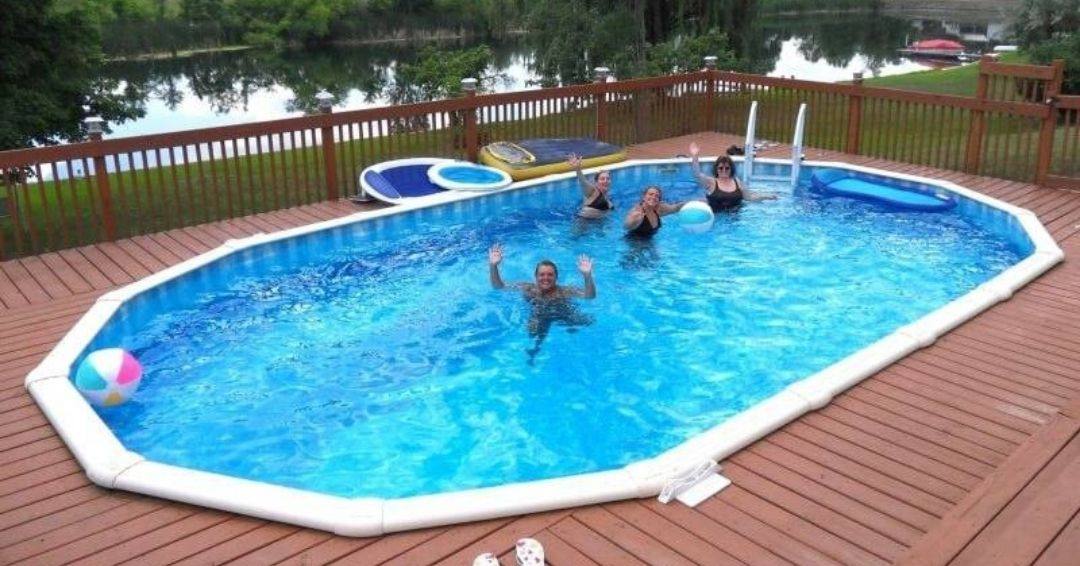 An above ground swimming pool surrounded by a wooden deck. There is a family swimming inside.