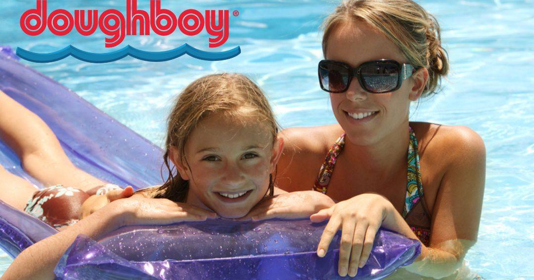 A mom is standing in an above ground pool next to her daughter who is laying on a pool float.